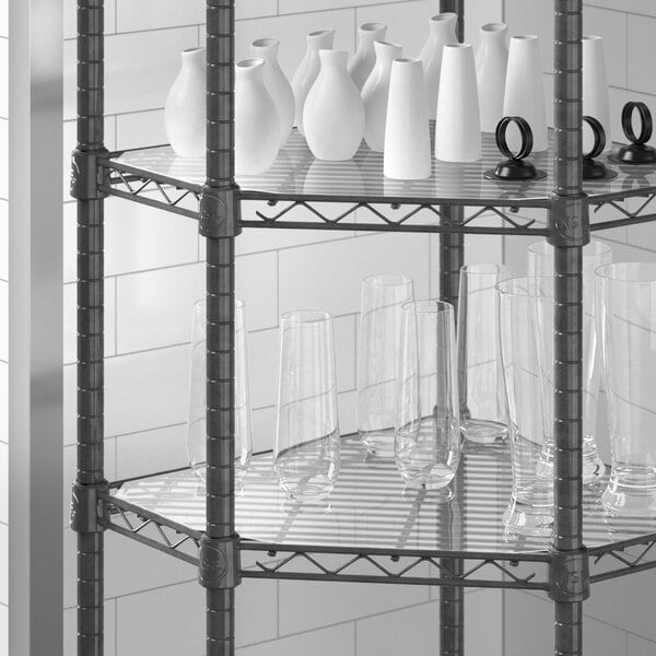 A Regency black metal corner shelf with clear PVC liner holding vases and glasses.