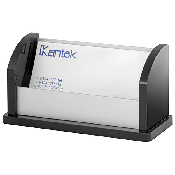 A black acrylic and aluminum Kantek business card holder on a desk with a business card inside.