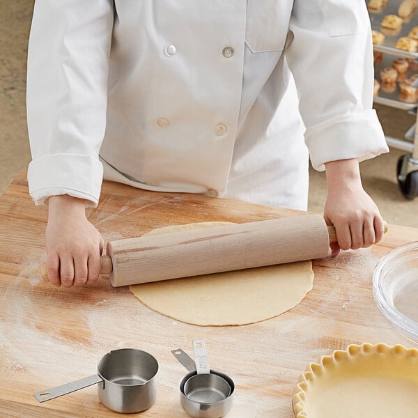 A person rolling out dough on a table with a Choice wood rolling pin.