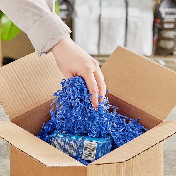 A hand holding Spring-Fill Royal Blue Crinkle Cut Paper Shred in a cardboard box.