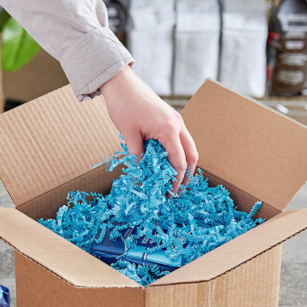 A hand holding Spring-Fill Light Blue shredded paper in a cardboard box.