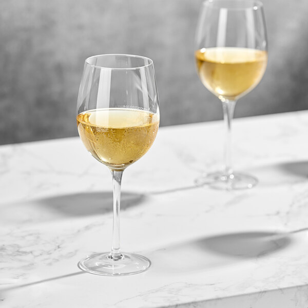 Two Della Luce Maia all-purpose wine glasses filled with white wine on a marble table.
