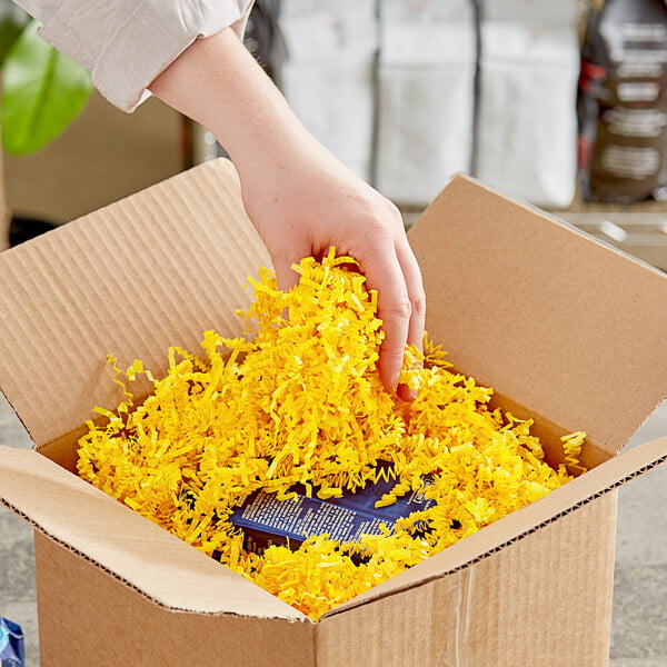A hand holding a cardboard box with yellow Spring-Fill paper shred.
