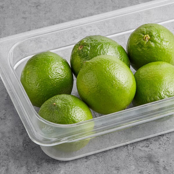 A plastic container filled with fresh limes on a counter.