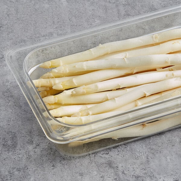 A glass container of fresh white asparagus on a table.