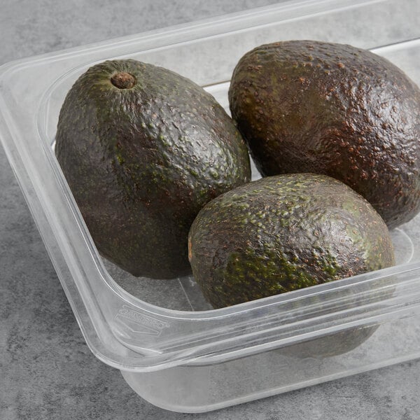 A plastic container of Fresh Hass Avocados on a glass surface.