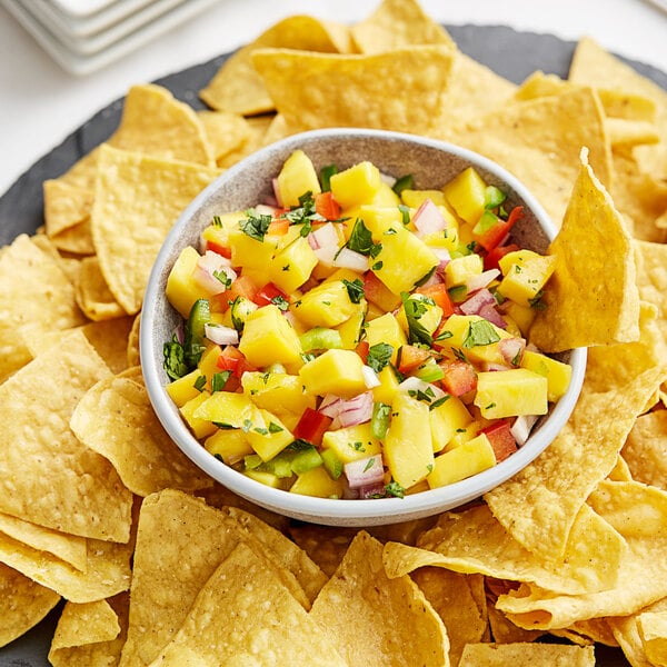 A bowl of fruit salsa on a plate of chips.