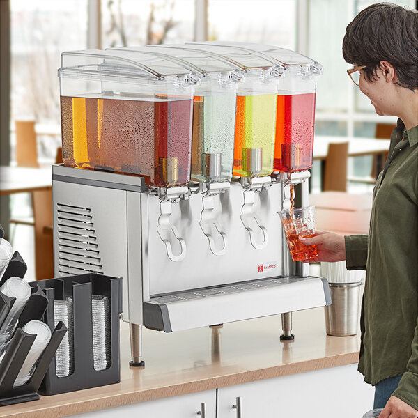 A man pouring liquid from a glass into a Crathco quadruple refrigerated beverage dispenser.