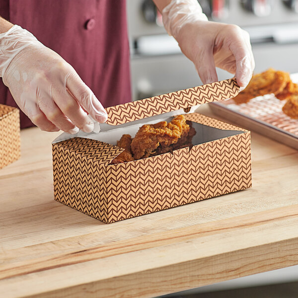 A person in gloves is putting fried chicken into a Choice Cornerstone take-out box.