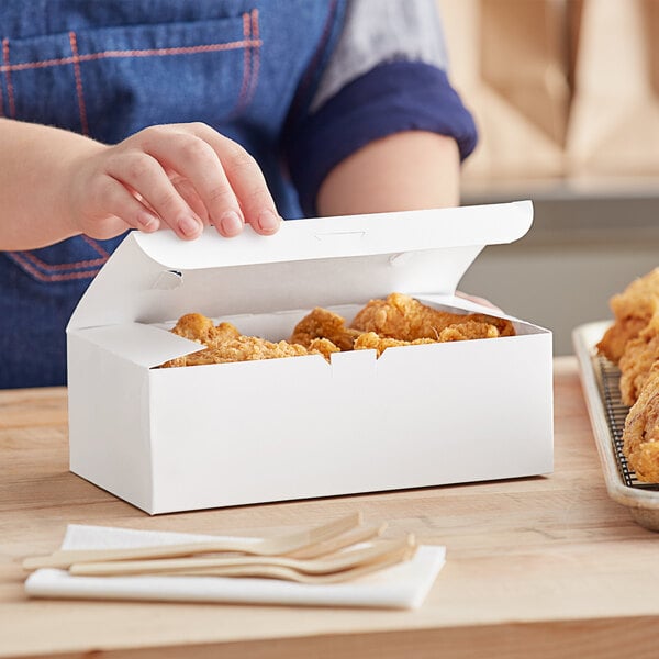 A person's hand reaching out to open a white Choice take out box of chicken.