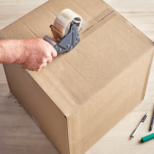 A hand using tape to seal a Lavex Kraft shipping box.