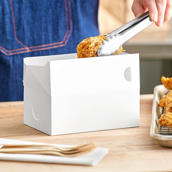 A person using tongs to put food in a white Choice take out box.