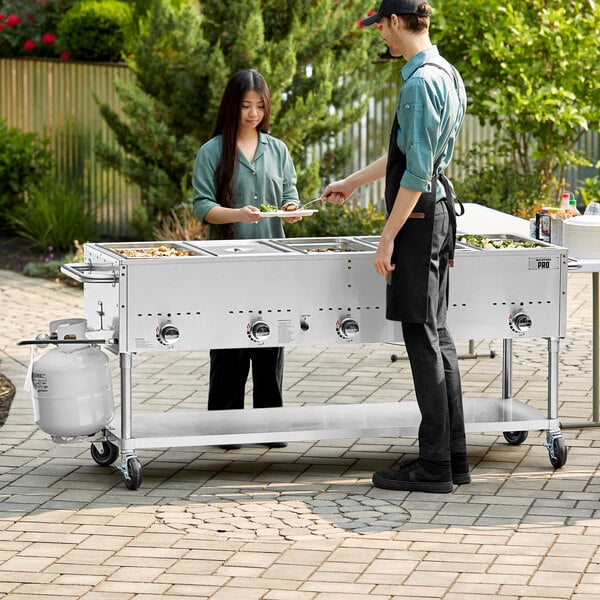 A man and woman using a Backyard Pro liquid propane steam table to serve food at an outdoor event.