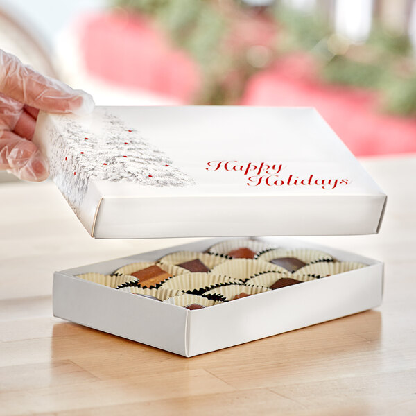 A gloved hand holding a Happy Holidays candy box filled with chocolates.