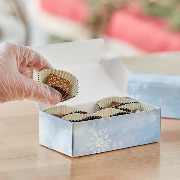 A gloved hand holding a 1 lb. snowflakes print candy box.