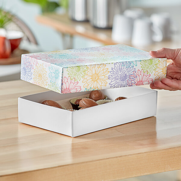 A hand holding a flowered 2-piece candy box with chocolates inside.