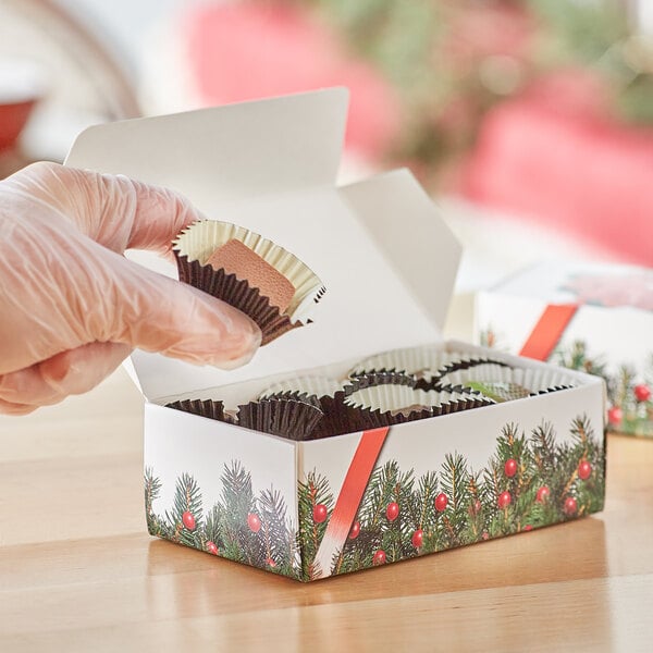 A gloved hand holding a Bow and Berries print candy box filled with chocolates.