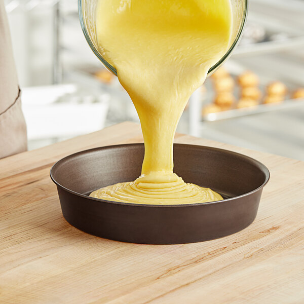 Batter being poured from a yellow bowl into a Gobel round cake pan.