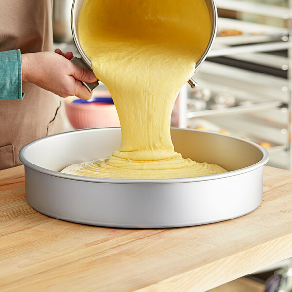 A woman pouring yellow cake batter into a Fat Daddio's round cake pan.