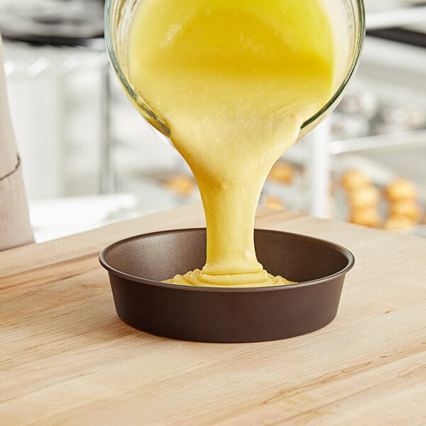 Yellow cake batter being poured into a Gobel round cake pan.
