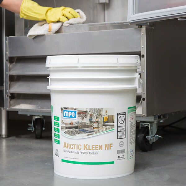 A white bucket of Arctic Kleen Ready-to-Use Freezer Cleaner with a yellow gloved hand