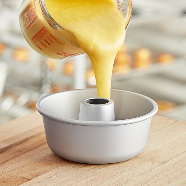A person pouring yellow liquid from a measuring cup into a Fat Daddio's ring cake pan.