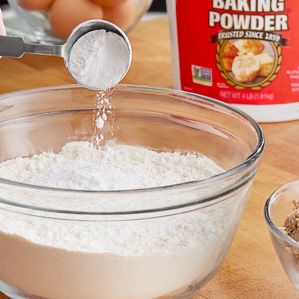 A person pouring Rumford Baking Powder into a bowl of flour.