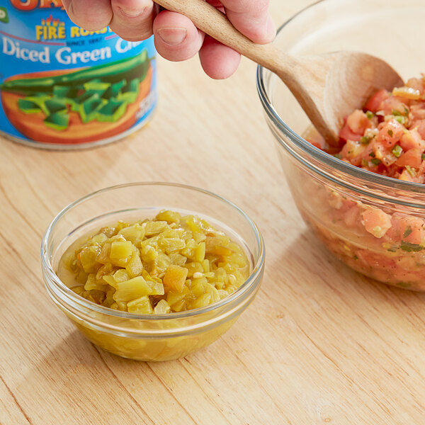 A hand holding a wooden spoon over a bowl of Ortega diced green chiles salsa.