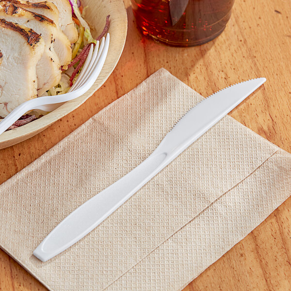 A Solo Impress white plastic knife on a napkin next to a plate of food.
