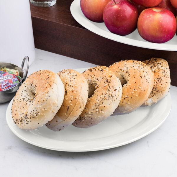 A Carlisle bone oval melamine platter with bagels and apples.