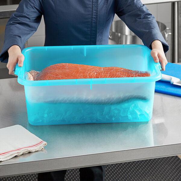 A woman in a blue shirt holding a Vigor blue polypropylene bus tub with a piece of meat inside.