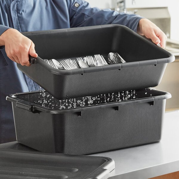 A man holding a black Choice polypropylene drain box filled with silverware.