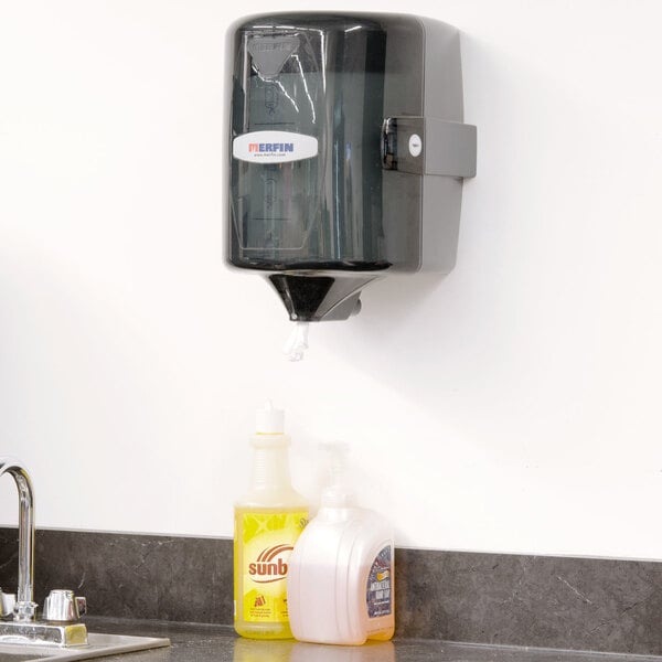 A Merfin smoke and grey center pull towel dispenser on a wall.