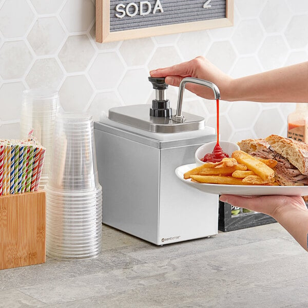A hand using a ServSense stainless steel condiment pump to pour ketchup on a plate of fries.