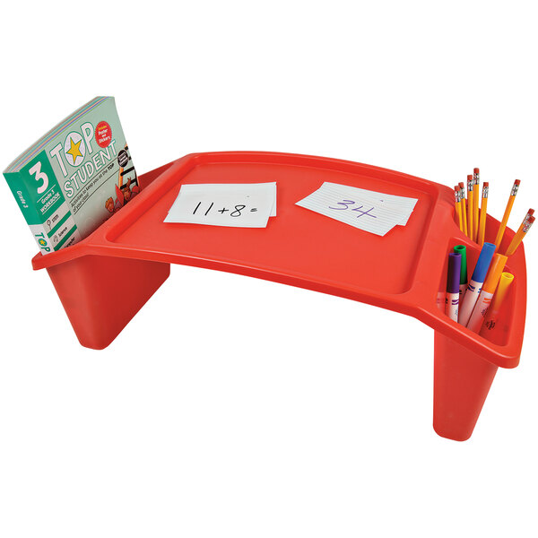 A red rectangular Deflecto kids lap tray on a desk with a book and pencils.