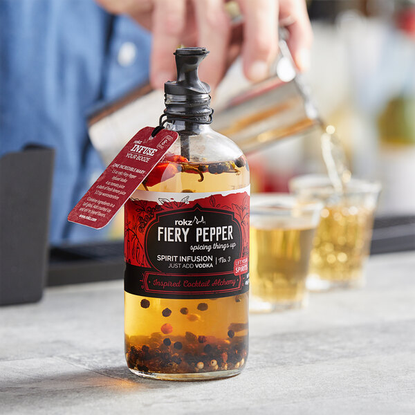 A bottle of Rokz Fiery Pepper liquid with a label being poured into a shot glass.