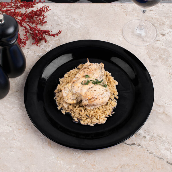 A Carlisle black narrow rim melamine plate with chicken and rice on a table.