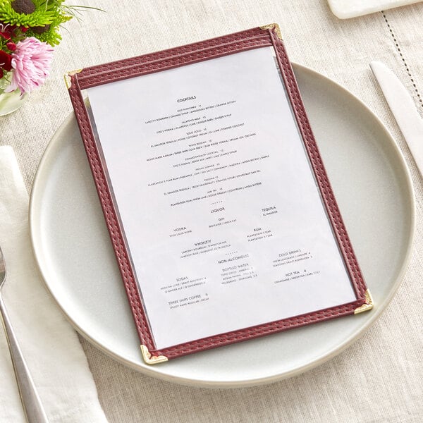A burgundy menu cover on a table with a plate and a fork.