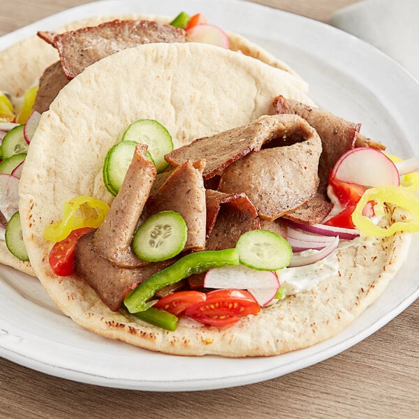 A plate with flatbread, Grecian Delight gyro meat, and vegetables on a table.