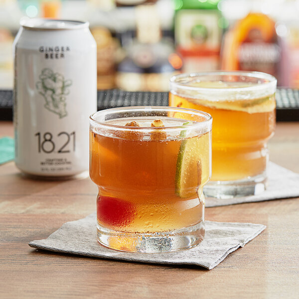 A glass of 18.21 Bitters Light Ginger Beer with ice and a lime slice on a napkin next to a beer can.
