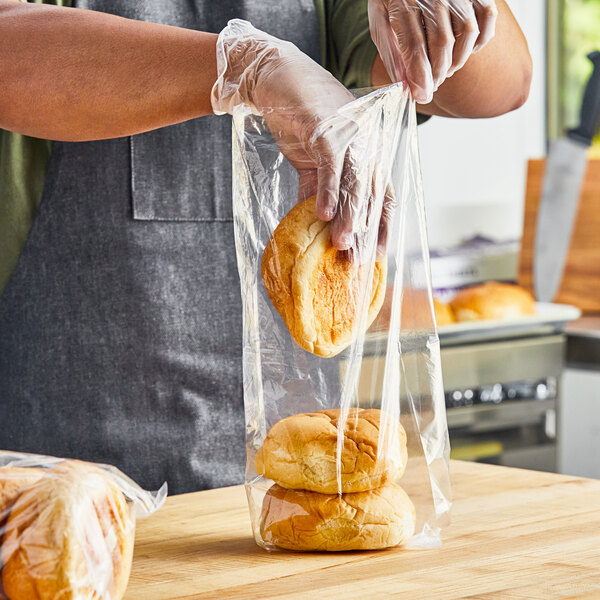A person wearing plastic gloves holding a Choice medium-duty plastic food bag filled with bread.
