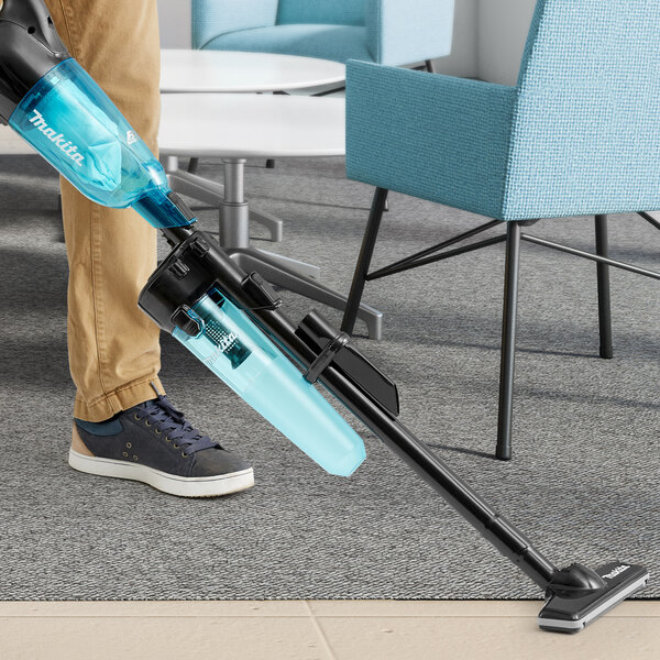 A person using a Makita stick vacuum to clean a carpet.