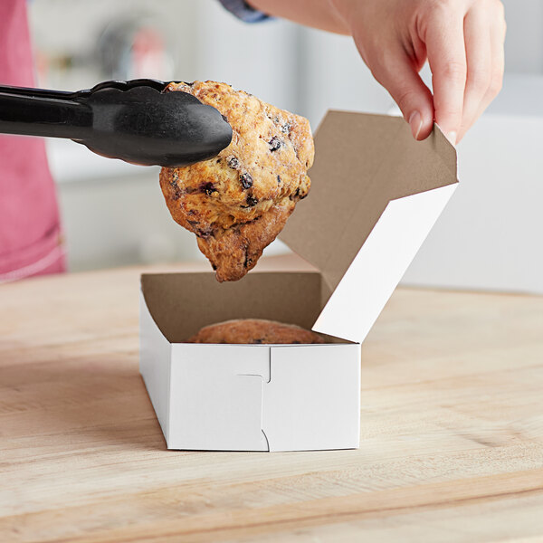A hand holding a scone in a white bakery box.