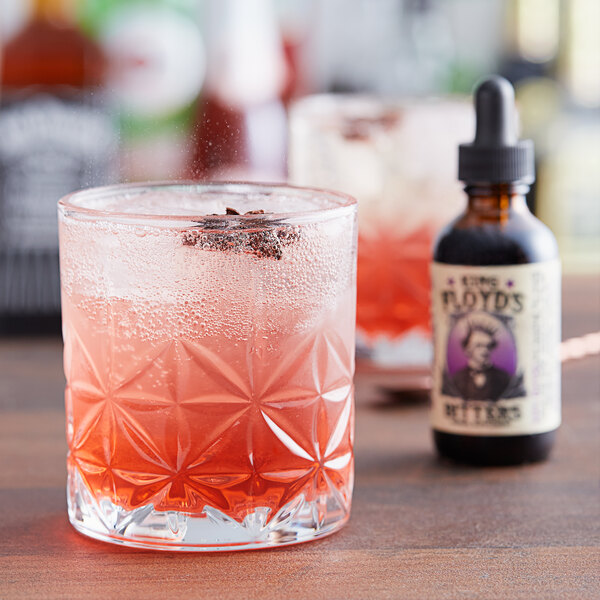 A glass of pink liquid with a brown bottle of King Floyd's Aromatic Digestive Bitters next to it.