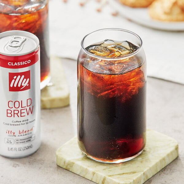 A can of illy cold brew coffee next to a glass of ice water on a table.
