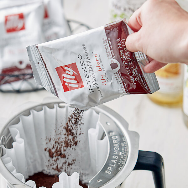 A hand pouring illy Intenso coffee from a packet into a coffee filter.