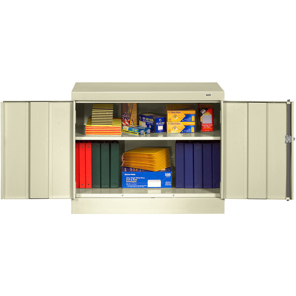 A Tennsco putty metal storage cabinet with books and folders on the shelf.