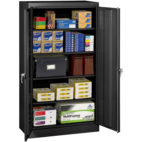 A black metal Tennsco storage cabinet with solid doors storing white boxes.
