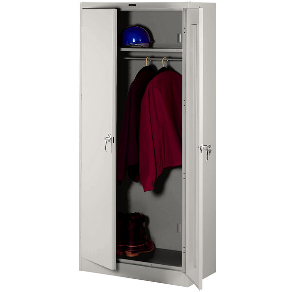 A light gray metal Tennsco wardrobe cabinet with solid doors holding a red jacket and hat.