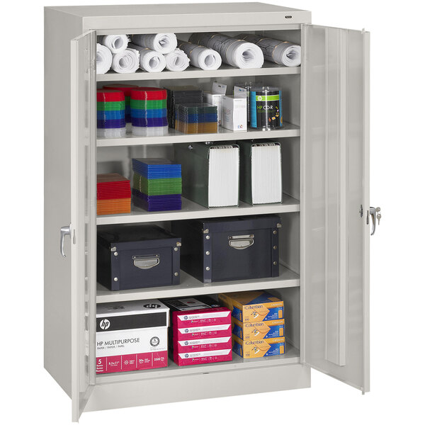 A Tennsco light gray storage cabinet with solid doors filled with boxes and rolls of paper.